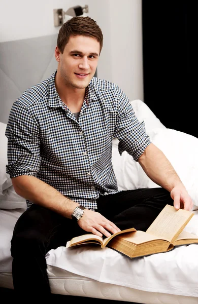 Un hombre con un libro en su cama . — Foto de Stock