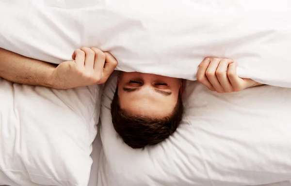 Hombre escondido en la cama bajo sábanas . — Foto de Stock