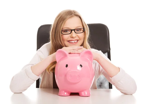 Ung kvinna med piggybank på skrivbordet — Stockfoto