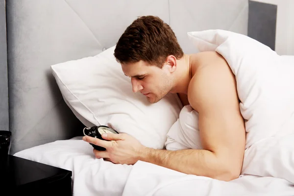 Mężczyzna z budzikiem w sypialni. — Zdjęcie stockowe