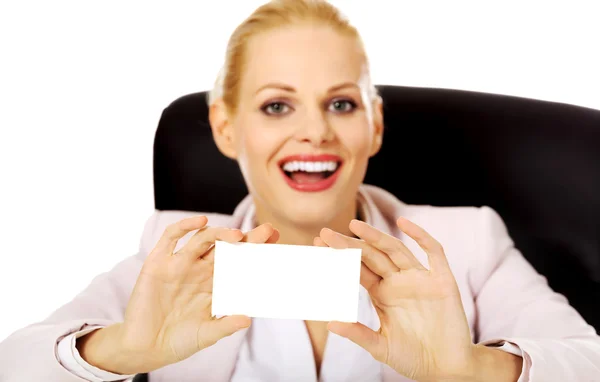 Smile business woman sitting behind the desk and holding empty buisiness card — Stock Photo, Image