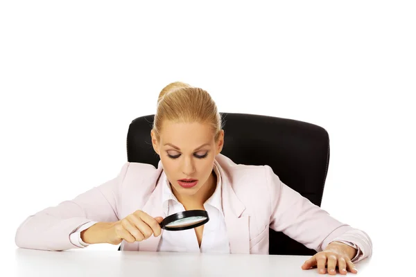 Mujer de negocios sentada detrás del escritorio y mirando una lupa — Foto de Stock