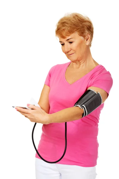 Старшая женщина измеряет артериальное давление с помощью автоматического манометра — стоковое фото