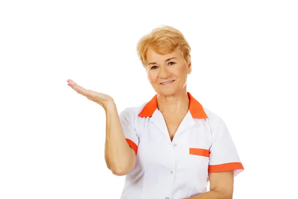 Smile elderly female doctor or nurse preseting something on open palm — Stock Photo, Image