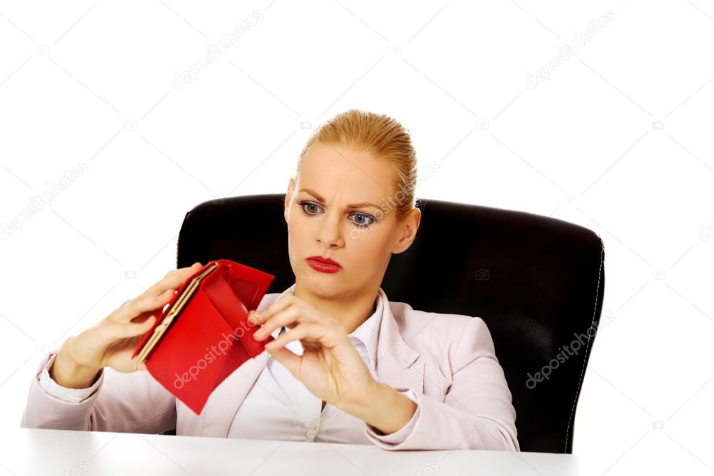 Worried business woman sitting behind the desk with empty wallet