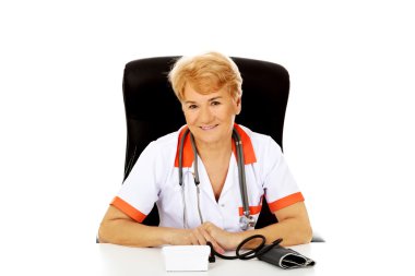Yaşlı kadın doktor veya hemşire oturma bloog basınç ölçer ile masanın arkasında gülümse