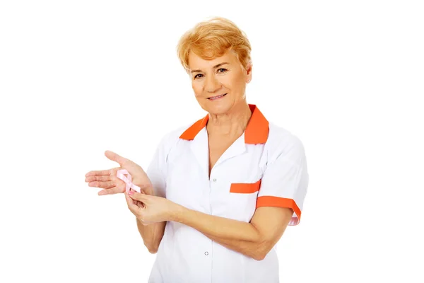 Elderly female doctor or nurse holds pink breast cancer awareness ribbon — Stock Photo, Image