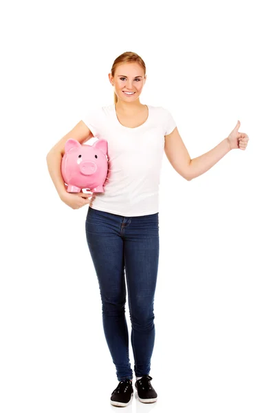 Happy young woman holding piggybank and showing thumb up — Stock Photo, Image