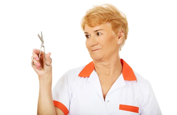 Улыбающаяся пожилая женщина-врач или медсестра с ножницами — стоковое фото