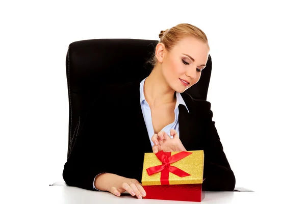 Mujer de negocios sonrisa abre una caja de regalo detrás del escritorio — Foto de Stock