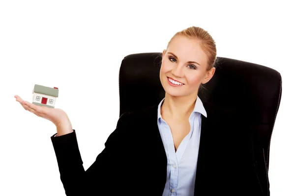 Smiling business woman sitting on a chair and holding house model — Stock Photo, Image