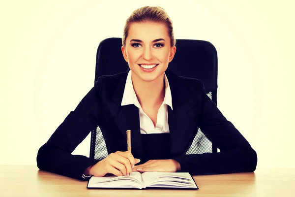 Sonriente mujer de negocios escribiendo nota junto a un escritorio —  Fotos de Stock