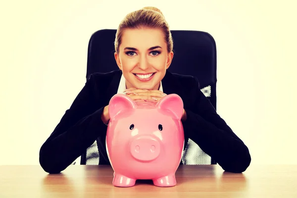 Businesswoman with a piggybank behind the desk — Stock Photo, Image