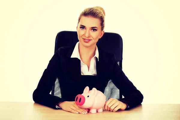 Affärskvinna med en piggybank bakom skrivbordet — Stockfoto