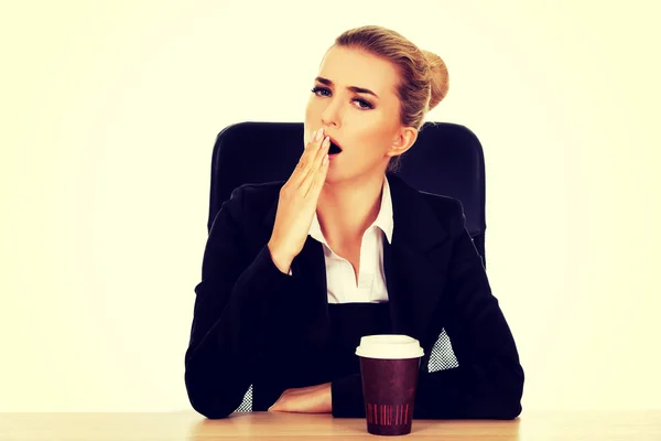 Empresaria bostezar beber café de la taza de papel detrás del escritorio —  Fotos de Stock