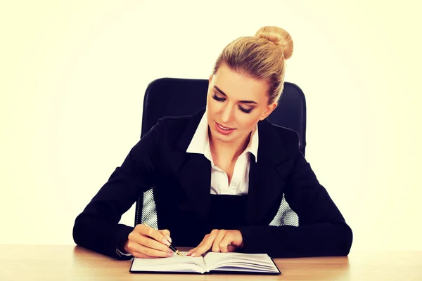 Sonriente mujer de negocios escribiendo nota junto a un escritorio —  Fotos de Stock