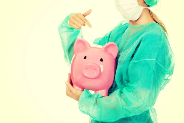 Female surgeon doctor holding piggy bank — Stock Photo, Image