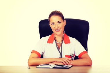 Sırıtma kadın doktor ya da hemşire masanın arkasında oturuyor.