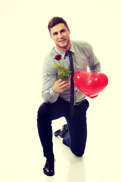 Hombre arrodillado con rosa roja y globo del corazón . — Foto de Stock