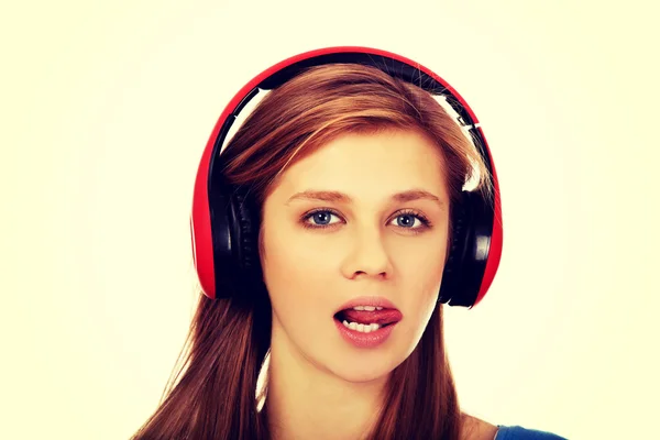 Teenage woman listens to music and shows tounge — Stock Photo, Image