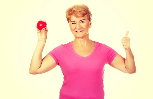 Oude lachende vrouw rode speelgoed hart met de duim te houden — Stockfoto