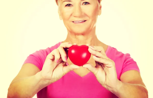 Viejo sonriente mujer sosteniendo rojo juguete corazón —  Fotos de Stock