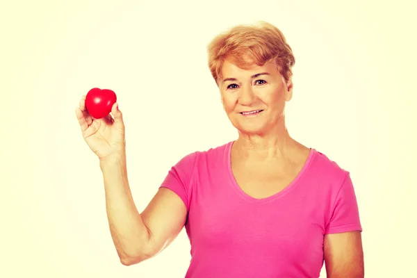 Old smiling woman holding red toy heart — Stock Photo, Image