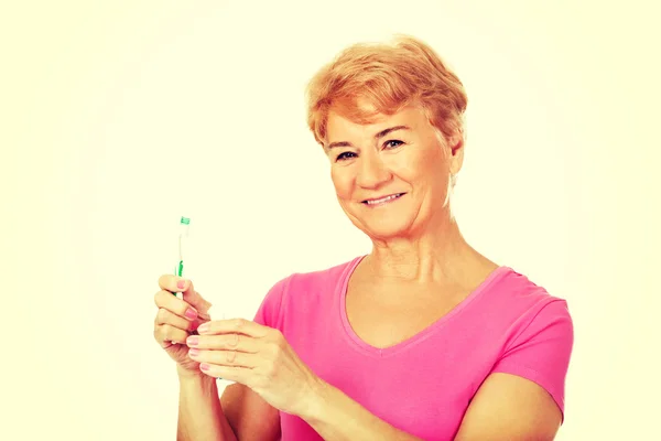 Sorrindo mulher idosa segurando pasta de dentes e escova de dentes — Fotografia de Stock