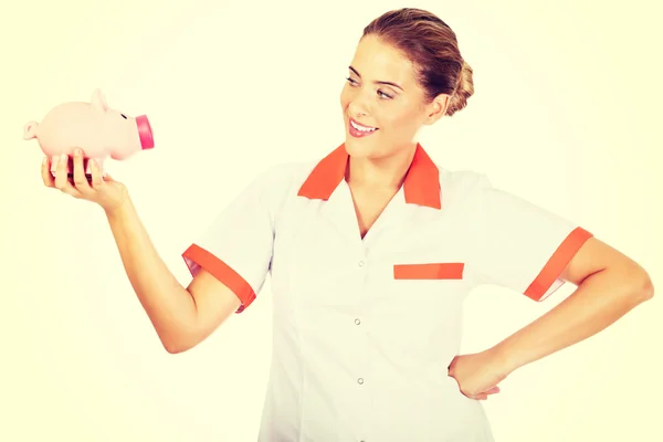 Junge schöne Ärztin oder Krankenschwester hält ein Sparschwein — Stockfoto