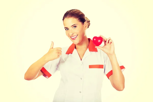 女医生或护士拿着玩具的心和节目大拇指 — 图库照片