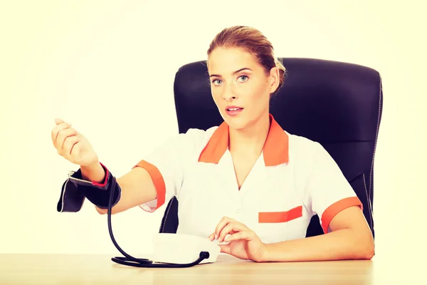 Doctor sitting behind the desk holding blood pressure gauge — Stock Photo, Image