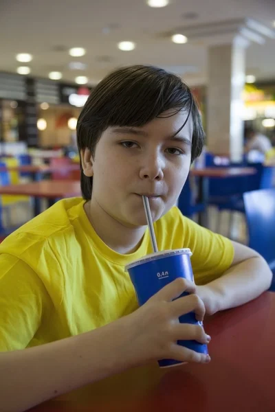 Boy with a beverage in a cafe in a shopping center — Stock Photo, Image