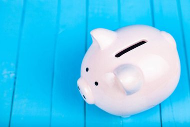 Mavi ahşap arka planda pembe domuz kumbarası.