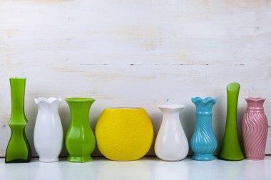 Beyaz ahşap arka planda sekiz farklı renkte çiçek vazosu..