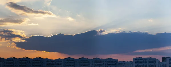 Beautiful sunset over the city. Clouds and sun over multi-storey buildings. Panorama.