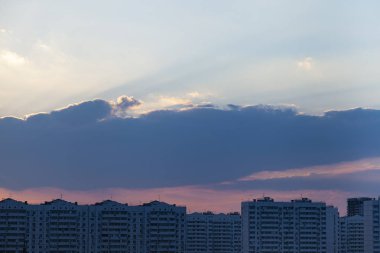 Şehrin üzerinde güzel bir günbatımı. Bulutlar ve güneş çok katlı binaların üzerinde.