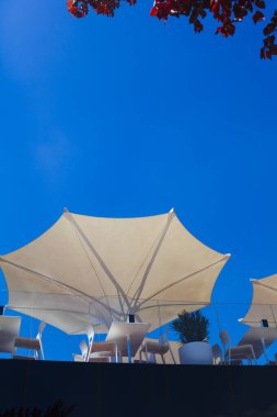Yazlık kafe. Mavi gökyüzüne karşı beyaz şemsiyeler ve masalar.