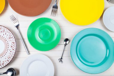 Ahşap zemin üzerinde çok renkli tabaklar, kaşıklar ve çatallar boş, üst görünüm.