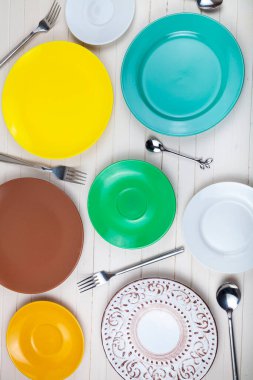 Ahşap zemin üzerinde çok renkli tabaklar, kaşıklar ve çatallar boş, üst görünüm.