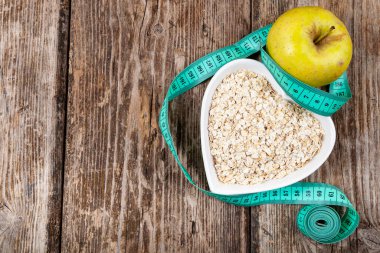 Kalp şeklinde bir tabakta yulaf ezmesi, yeşil elma ve mezura. Kilo kaybı ve diyet konsepti.