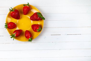 Tahta bir arka planda sarı bir tabakta olgun çilekler..