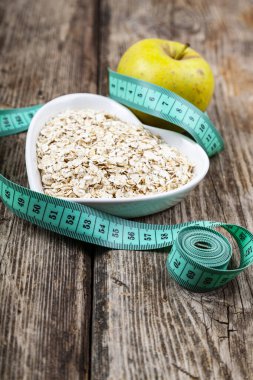 Kalp şeklinde bir tabakta yulaf ezmesi, yeşil elma ve mezura. Kilo kaybı ve diyet konsepti.