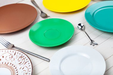 Ahşap zemin üzerinde çok renkli tabaklar, kaşıklar ve çatallar boş, üst görünüm.