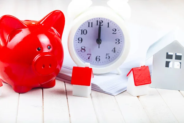 Pig piggy bank and small houses on the background of the clock. Time to save up for real estate.
