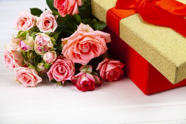 Ahşap arka planda kırmızı bir kutuda pembe güller. Çiçekli tebrik kartı.