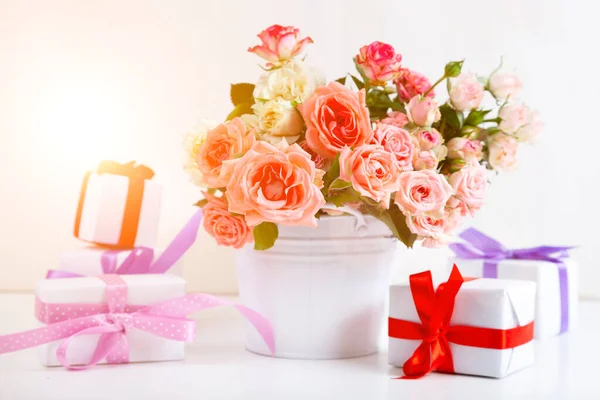Bouquet of pink roses and boxes with gifts on a light wooden background.