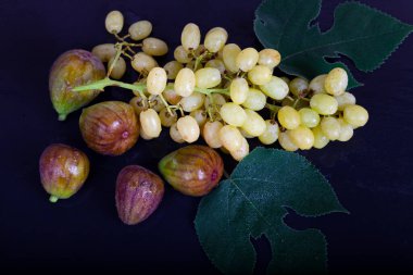 Siyah arka planda incir, üzüm ve yapraklar.