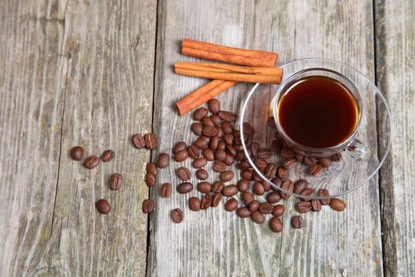 Transparent cup of coffee, beans and cinnamon sticks — Stock Photo, Image