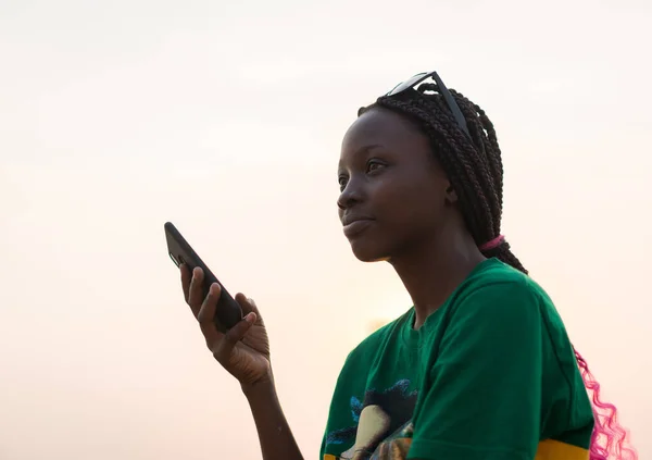 Młoda piękna czarna dziewczyna za pomocą smartfona na plaży morskiej o zachodzie słońca — Zdjęcie stockowe
