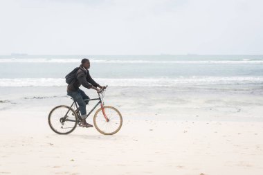 Afrikalı adam tropikal plajda bisiklet sürüyor.